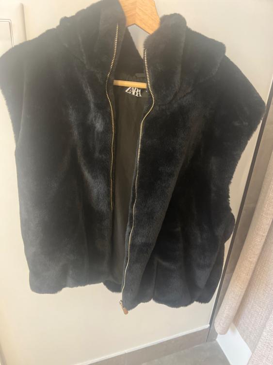 Black plush vest with hood and gold zipper, hanging on a wooden hanger. Visible tag: ZARA.