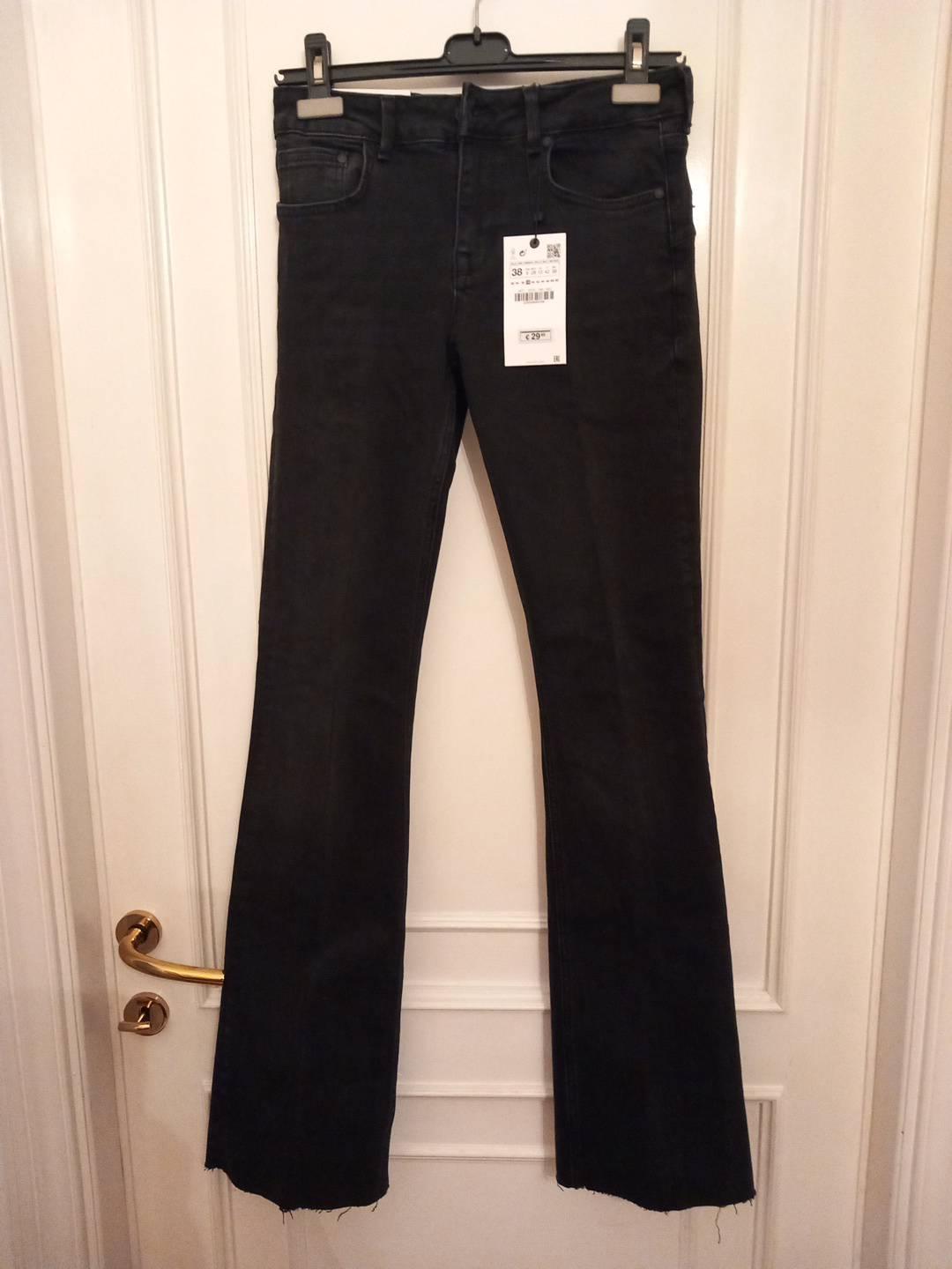 Black flared jeans with frayed hems on a hanger against a white door with a gold handle. Label with text 38 and €29.