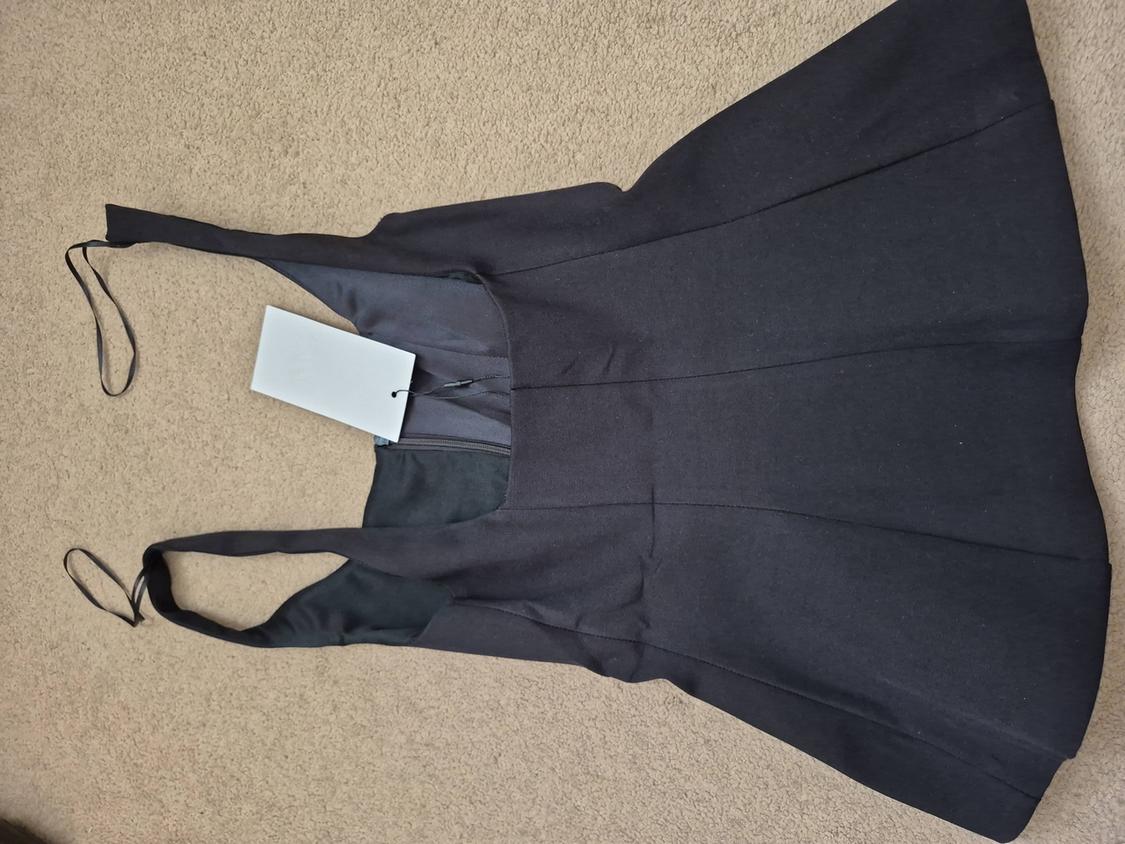Sleeveless black dress with spaghetti straps, white tag hanging, on a beige rug.