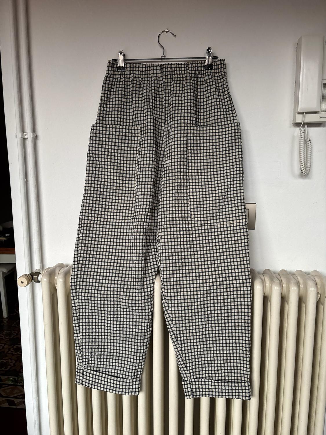 Black-and-white checked trousers with an elasticated waist, hanging over a radiator against a white wall. A relaxed domestic setting.