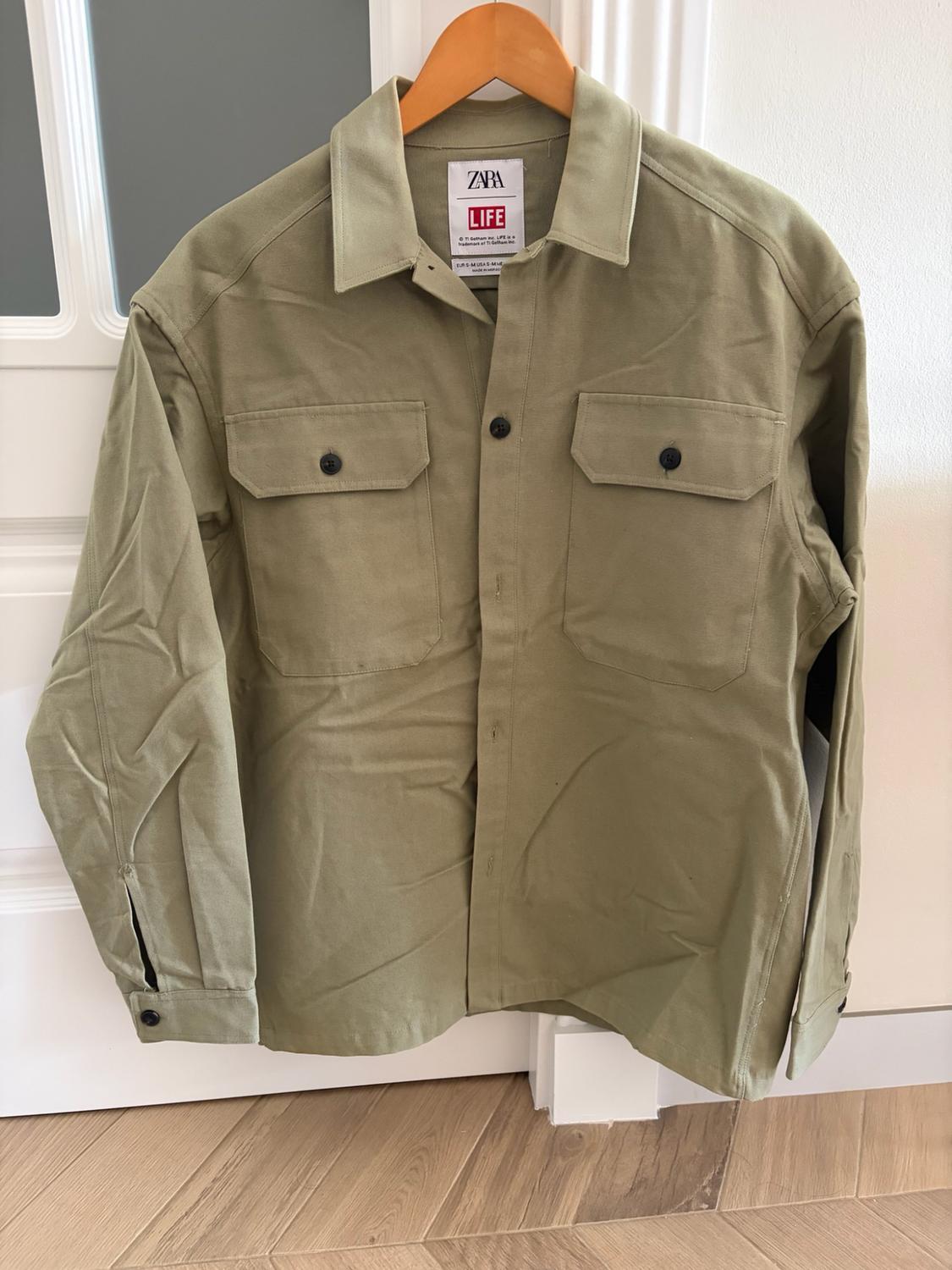 Green button-up overshirt with chest pockets, hanging on a wooden hanger. Label with the text ZARA LIFE.