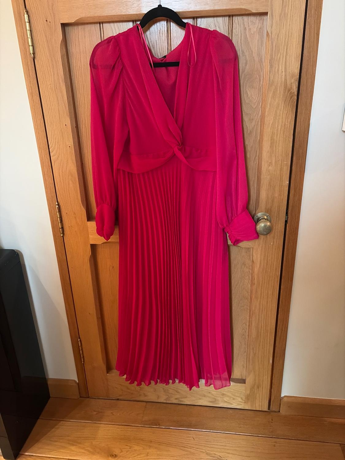 Red long-sleeved pleated dress hanging on a wooden door.