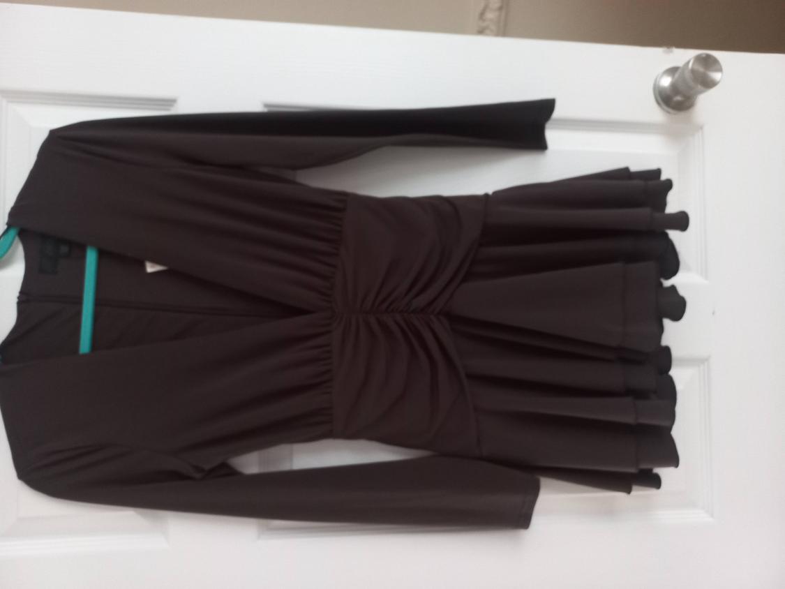 Dark long-sleeved dress with a V-neckline, gathered waist and pleated skirt, hanging on a white door.