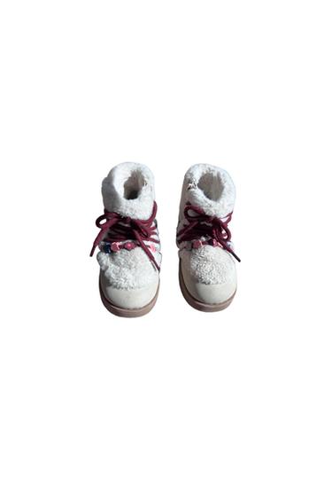 Infant white booties with a plush texture, burgundy laces, and small floral decorative details on the front.