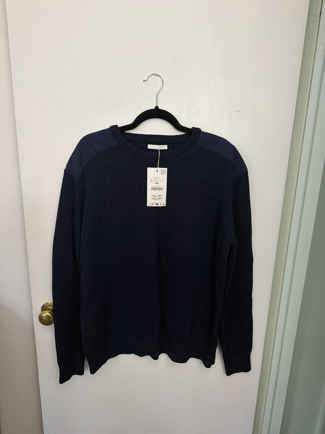 Navy blue knit jersey with shoulder patches and a label, hanging on a black hanger over a white door with a golden doorknob.