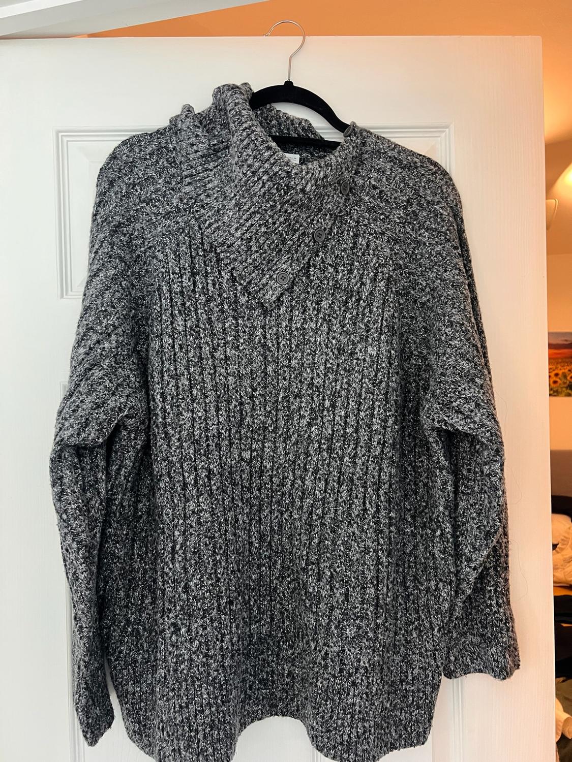 Grey marl chunky knit jumper with a high neck and buttons, hanging on a black hanger over a white door. Relaxed atmosphere.