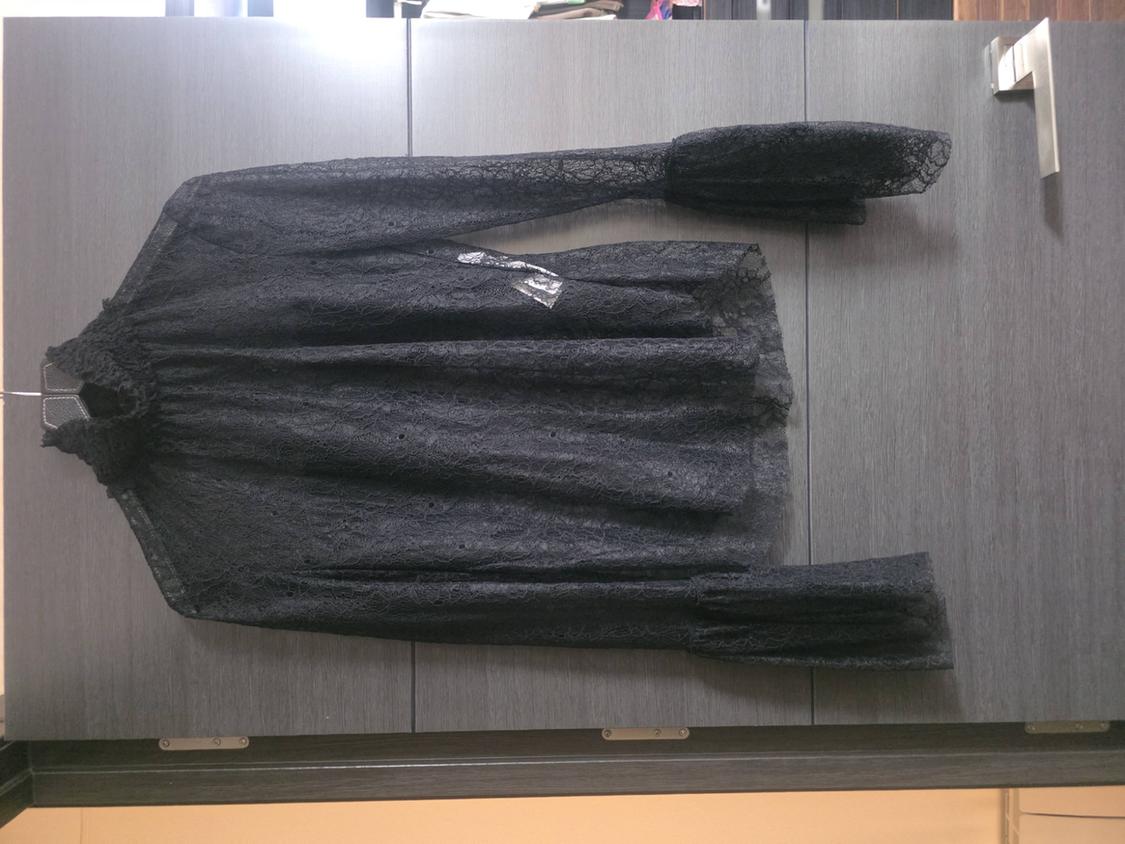 Black sheer lace blouse, high neck and flared sleeves, hanging on a grey wardrobe door.