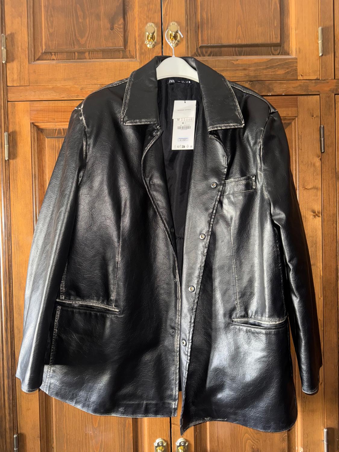 Worn black jacket with buttons hanging in a wooden wardrobe. Visible text: ZARA, WASHED EFFECT, M, € 79.95.