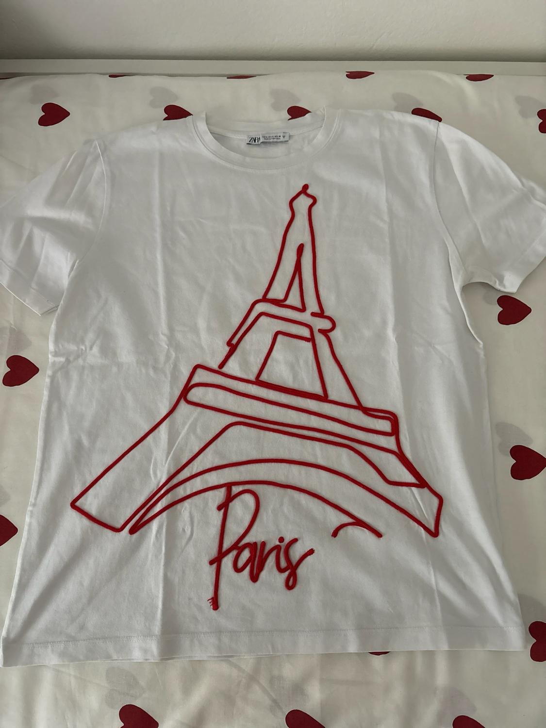 Λευκό T-shirt με κόκκινο σχέδιο του Πύργου του Άιφελ και κείμενο Paris, σε λευκό φόντο με μοτίβο από κόκκινες καρδιές.