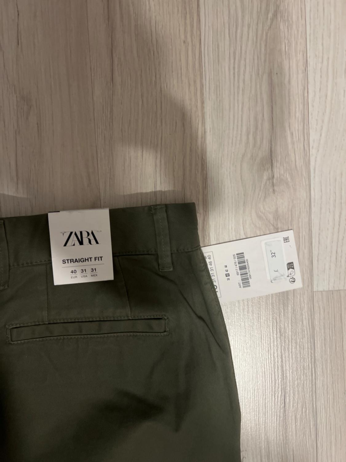 Olive green straight-cut trousers on a light wooden floor. Visible label: "ZARA STRAIGHT FIT 40 31 31 EUR USA MEX".