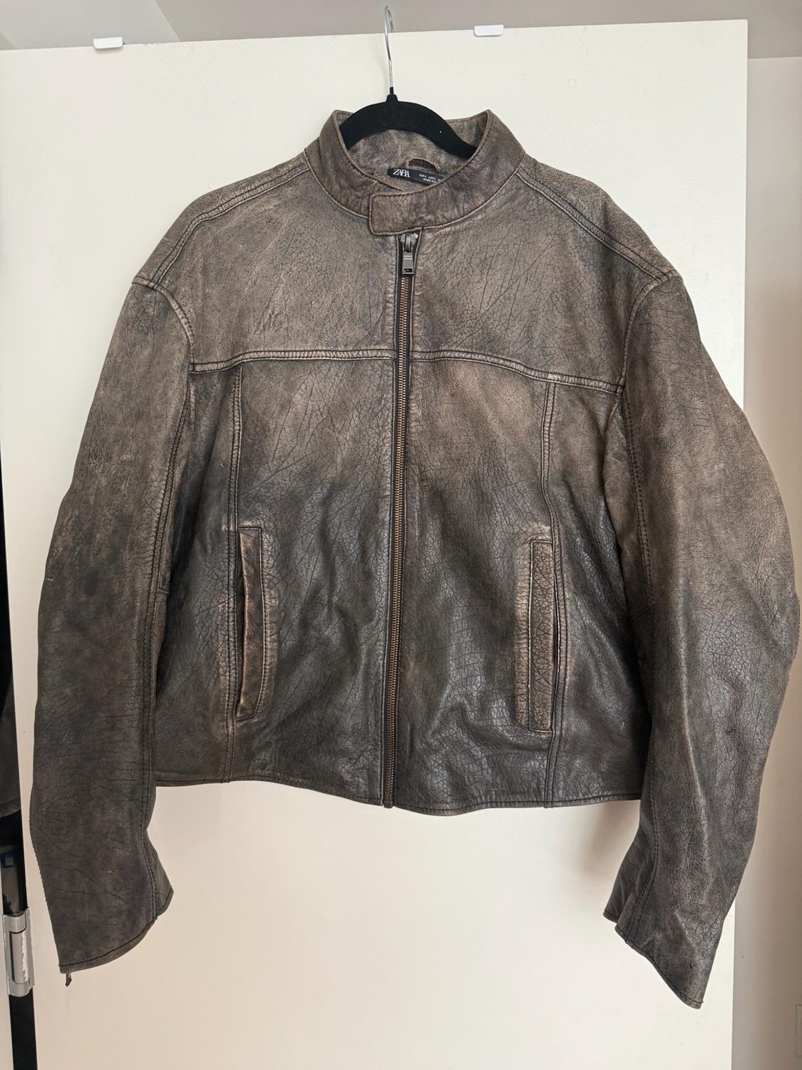 Distressed brown jacket hanging on a black hanger against a white background. Zipper closure and ZARA label on the collar.