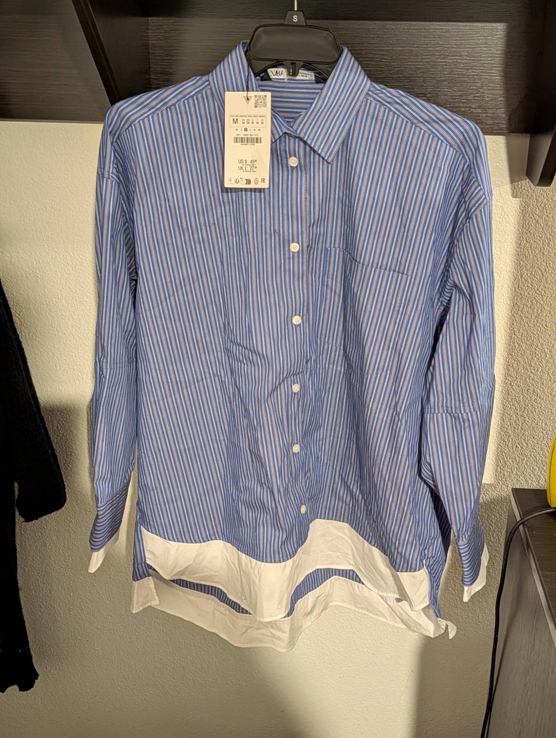 Blue and white striped shirt hanging on a black hanger, with a visible price tag. Light wall background.