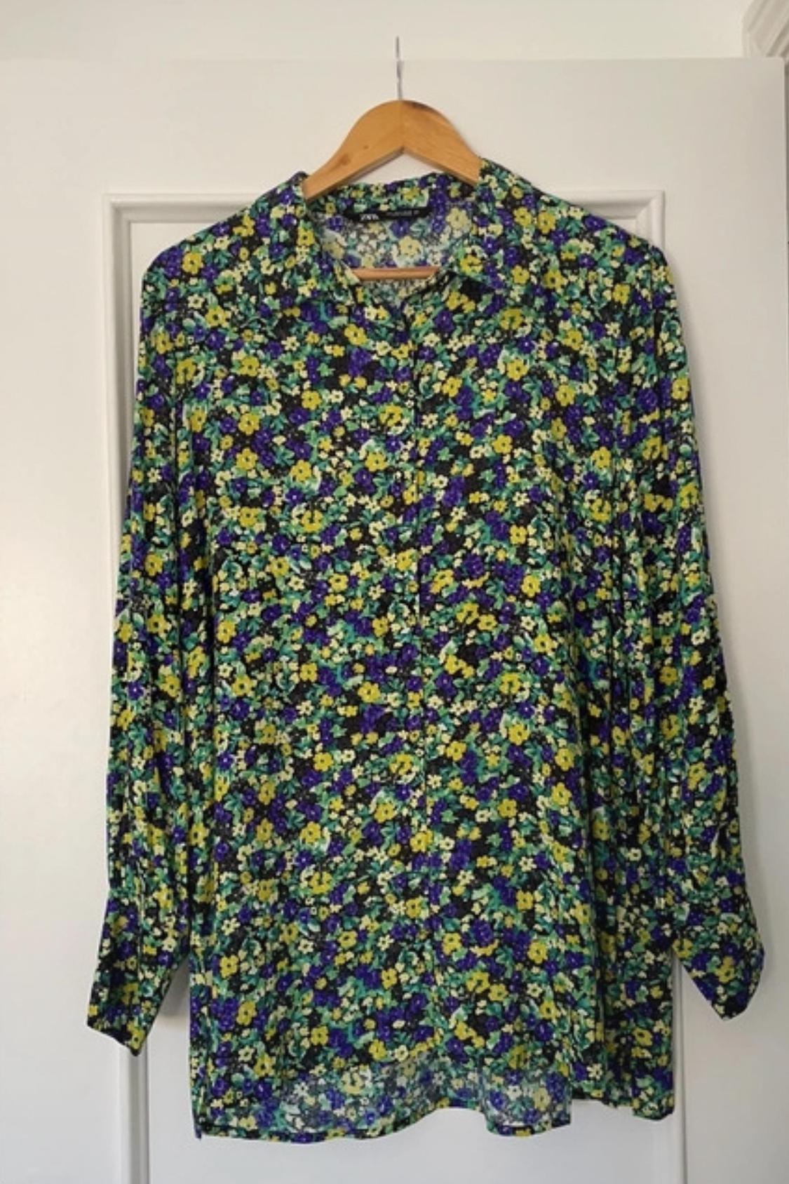 Front view of a floral print blouse in shades of purple, yellow and green, with a classic collar and long sleeves.