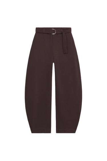 Front view of brown pants with wide leg, mid-rise, and adjustable belt with metal buckle.