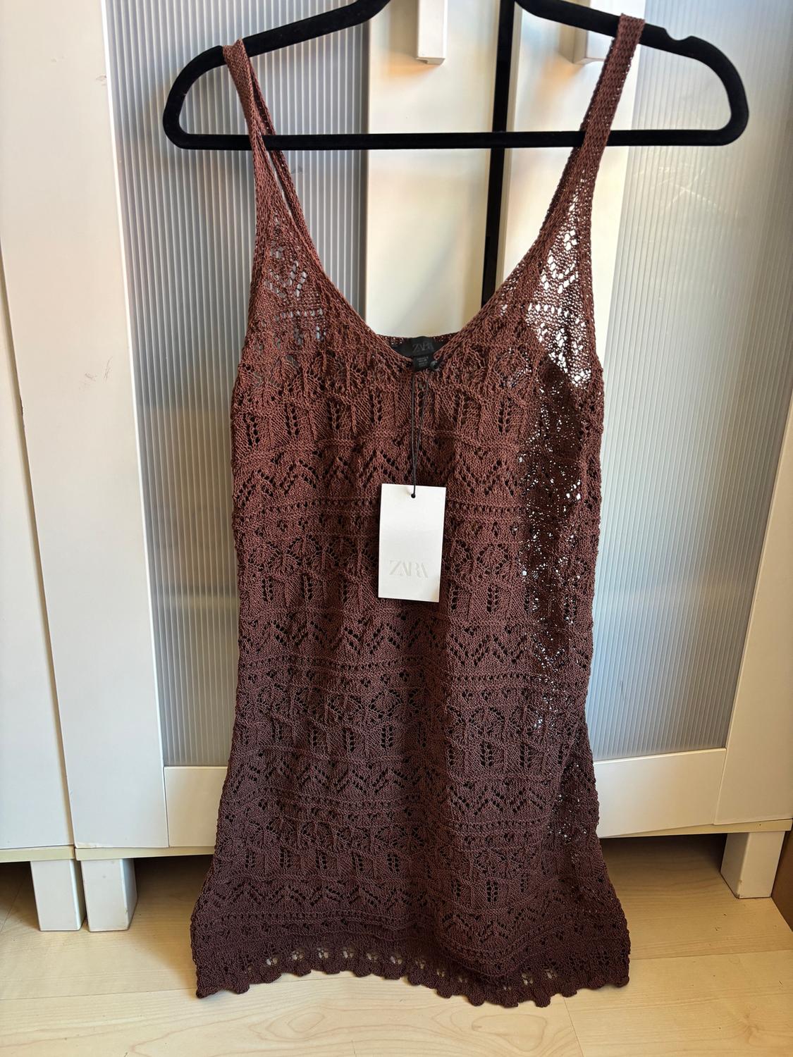 Brown crochet dress hanging on a black hanger, with a visible Zara tag, against a white wardrobe background.