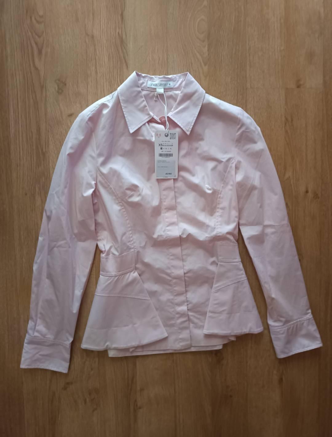Pink long-sleeved shirt with a peplum hem on a wooden floor. Visible label with the text ZARA, XS, €45.95.