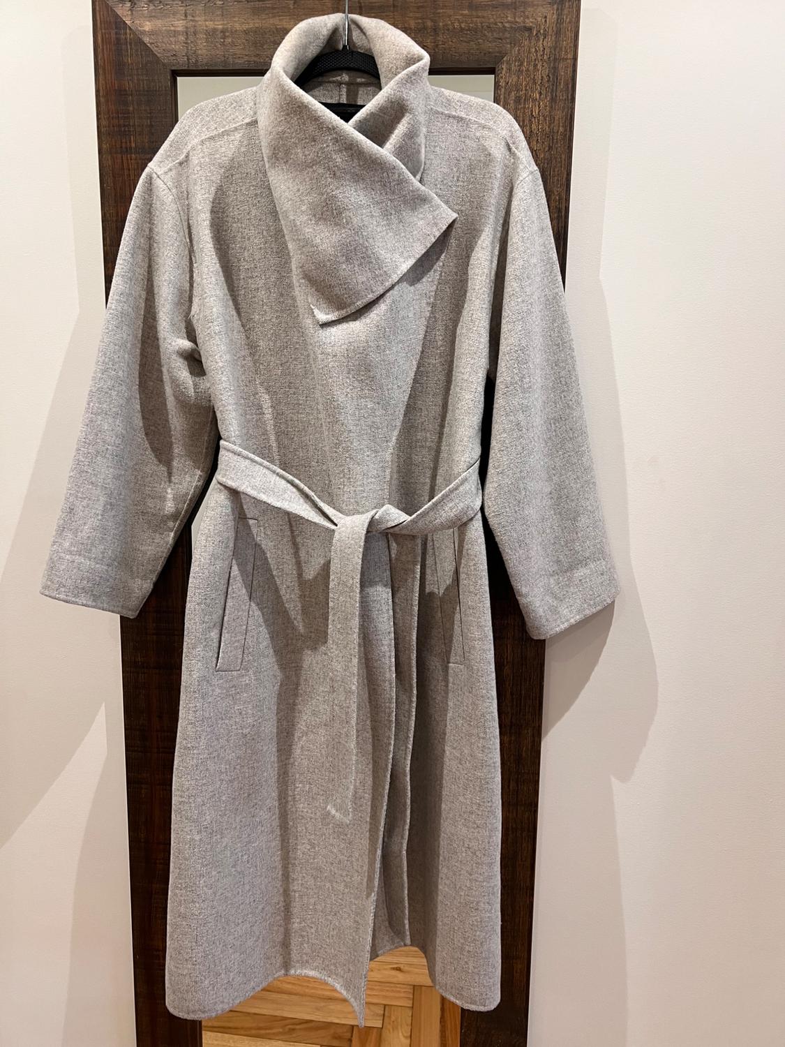Light grey coat hanging on a wooden hanger, with a high collar and matching belt, on a white background.