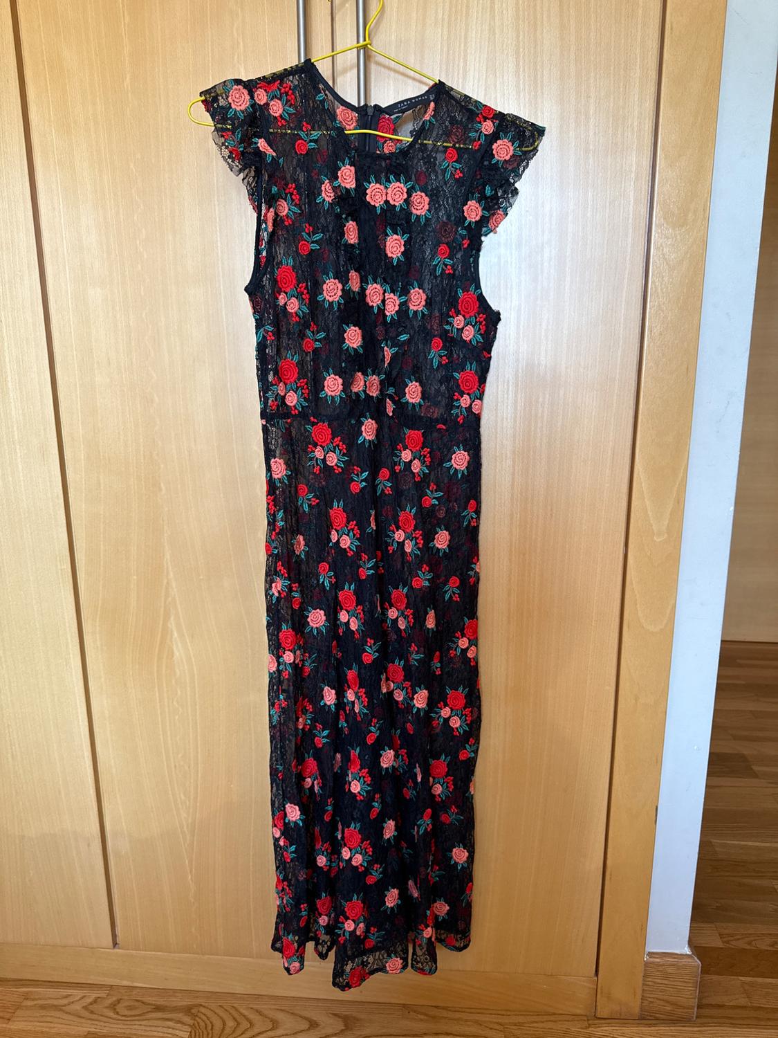 Front view of a black long dress with a red and pink floral print, sleeveless, with a back fastening.