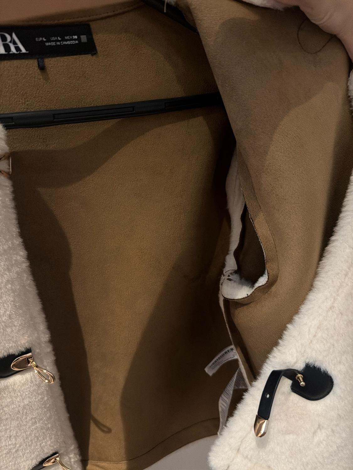 Close-up of the inside of a brown jacket with a white fleece outer. Text: EUR L USA L MEX 30 MADE IN CAMBODIA.