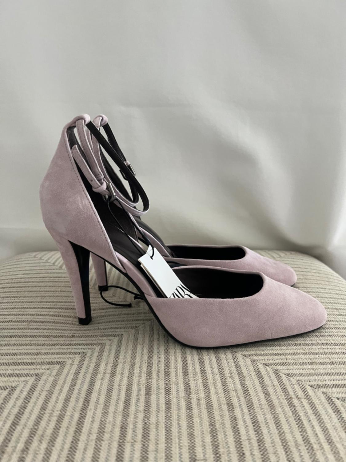 Lilac high-heeled shoes with ankle straps, displayed on a geometric patterned fabric and a white cloth background.