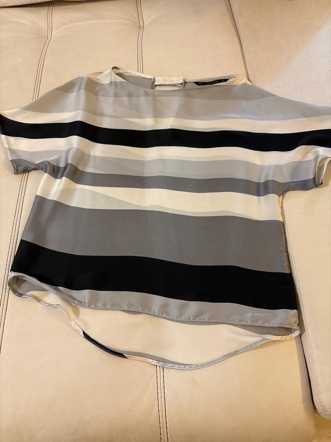 Short-sleeved blouse with a horizontal stripe pattern in shades of grey, white, and black, on a light beige background.
