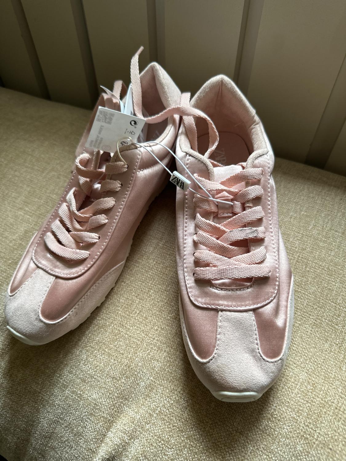 Pink trainers with laces and a satin finish on a beige fabric surface. Visible label with the text ZARA.