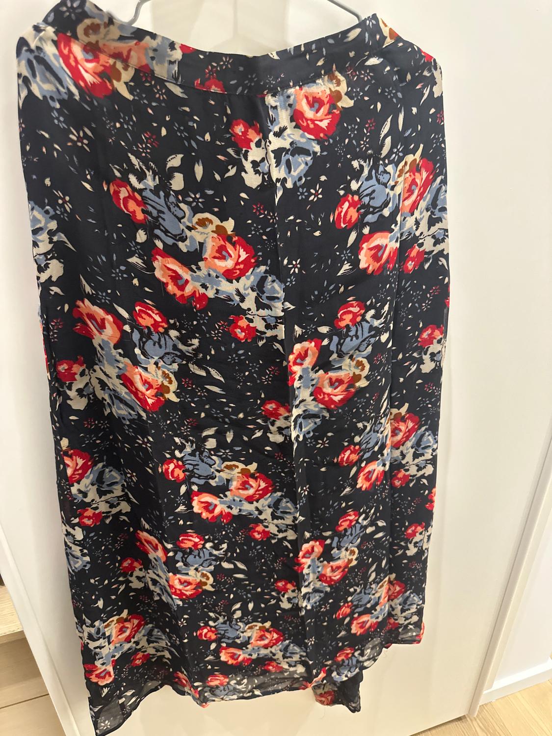 Hanging skirt with floral print in red, blue, and beige tones on a black background, hanging on a white hanger.