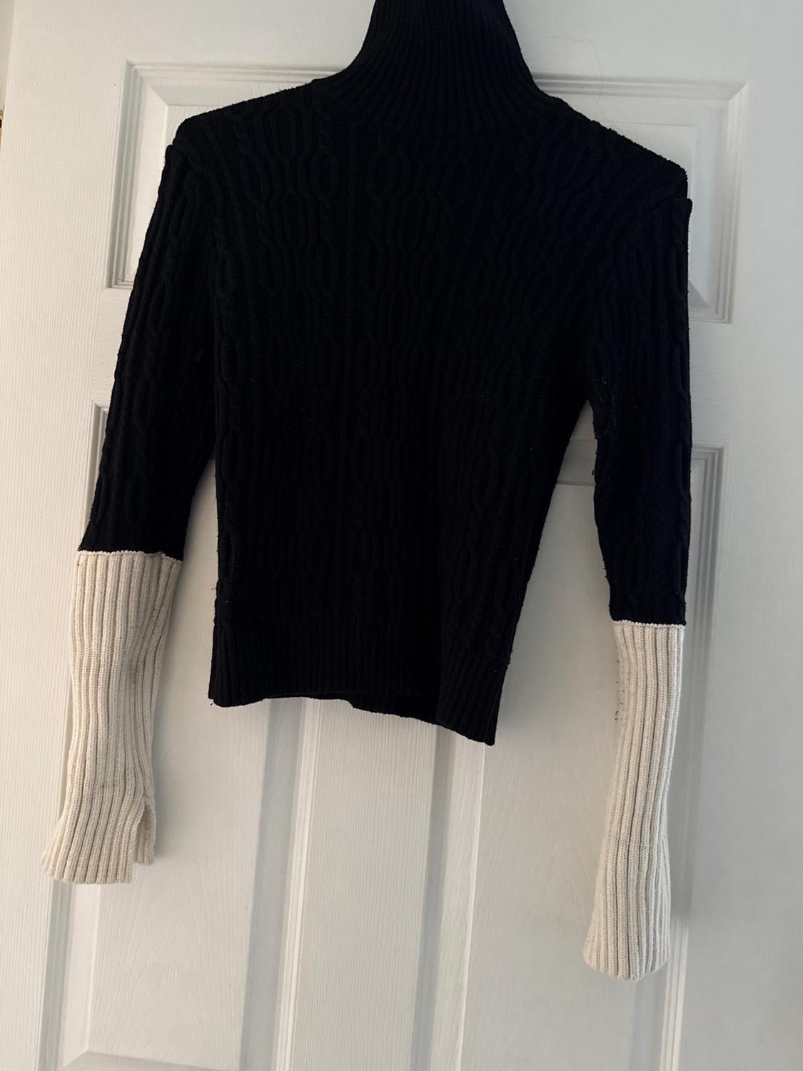 Black turtleneck sweater with long white contrasting sleeves, hanging on a white door.