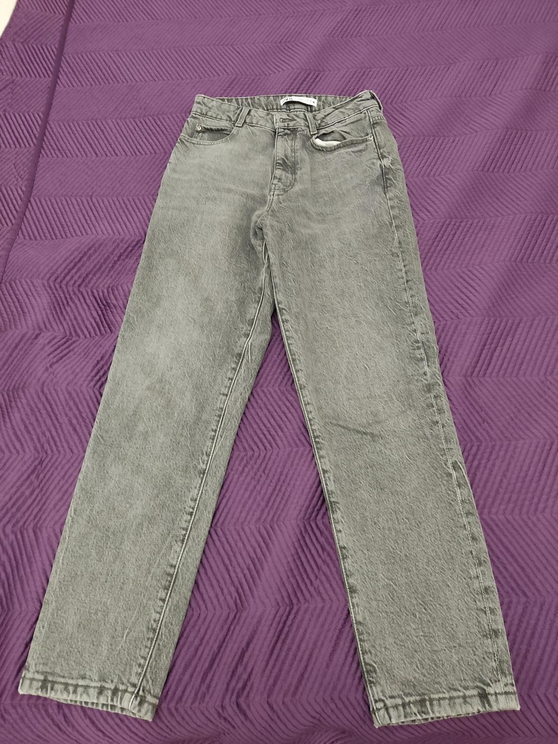 Grey jeans laid out on a purple quilt with a geometric pattern.