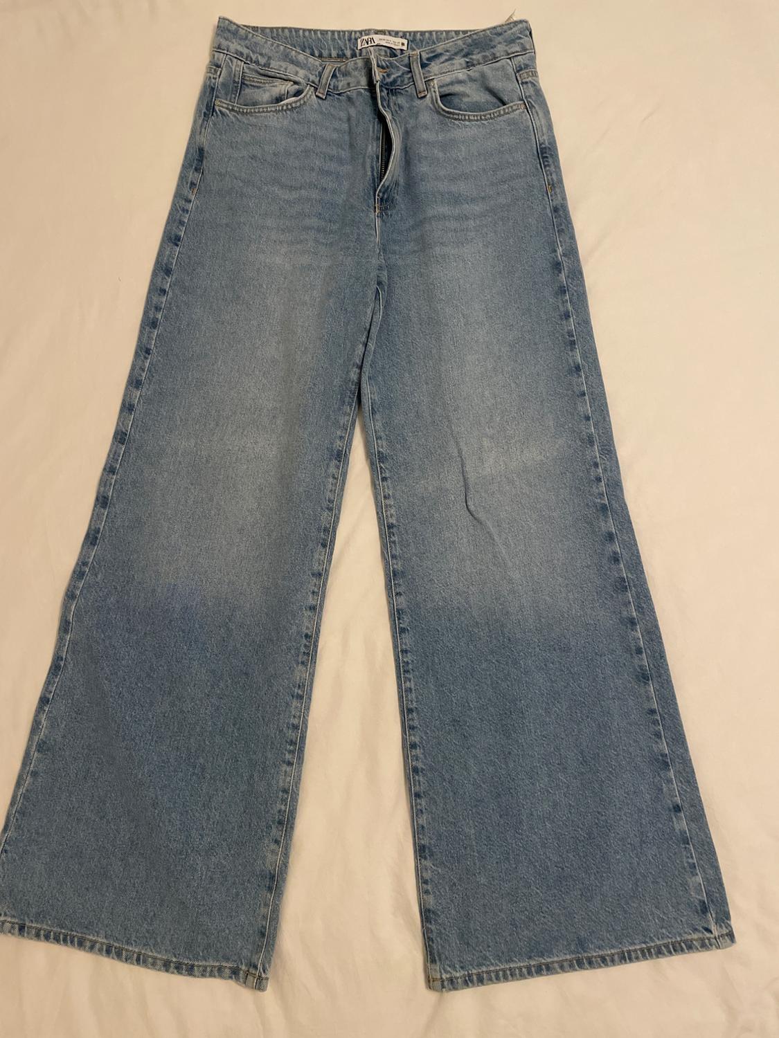 Light blue denim wide-leg jeans, with front and back pockets, on a beige background.