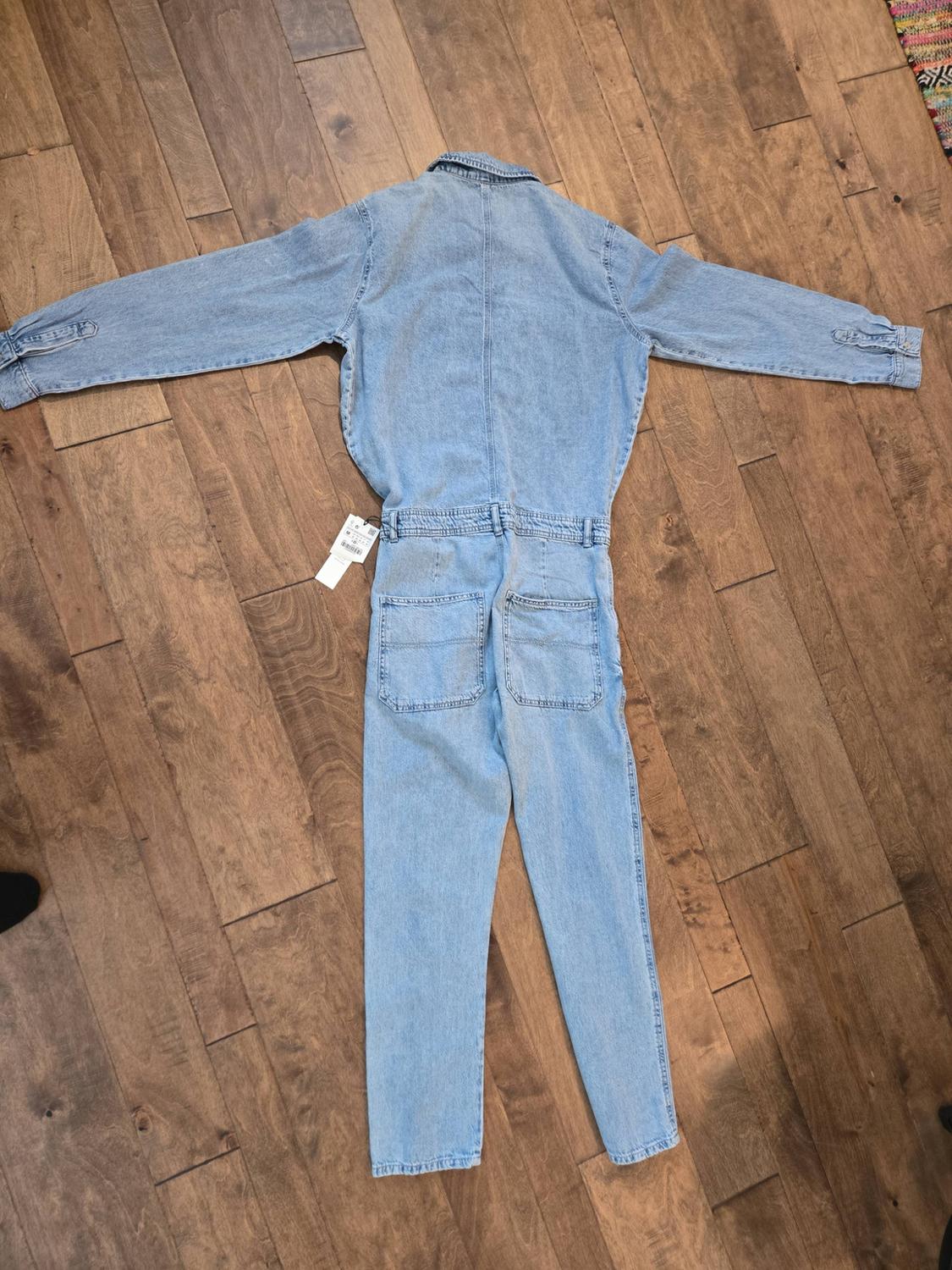 Light blue denim jacket laid out on a wooden floor, showing the back with long sleeves, two pockets, and a label.
