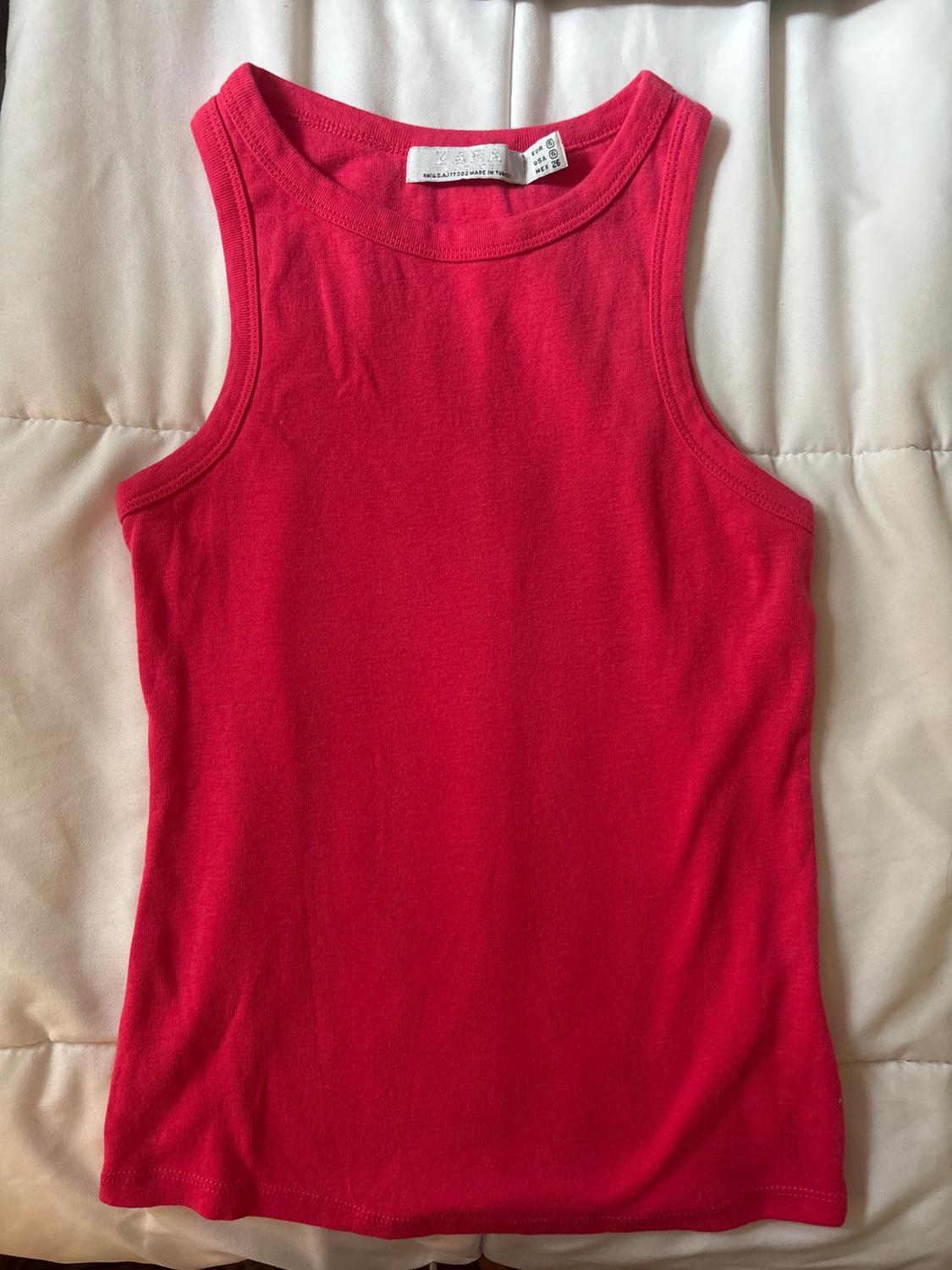Pink sleeveless top on a white fabric surface. Visible label with the text ZARA. Casual style.