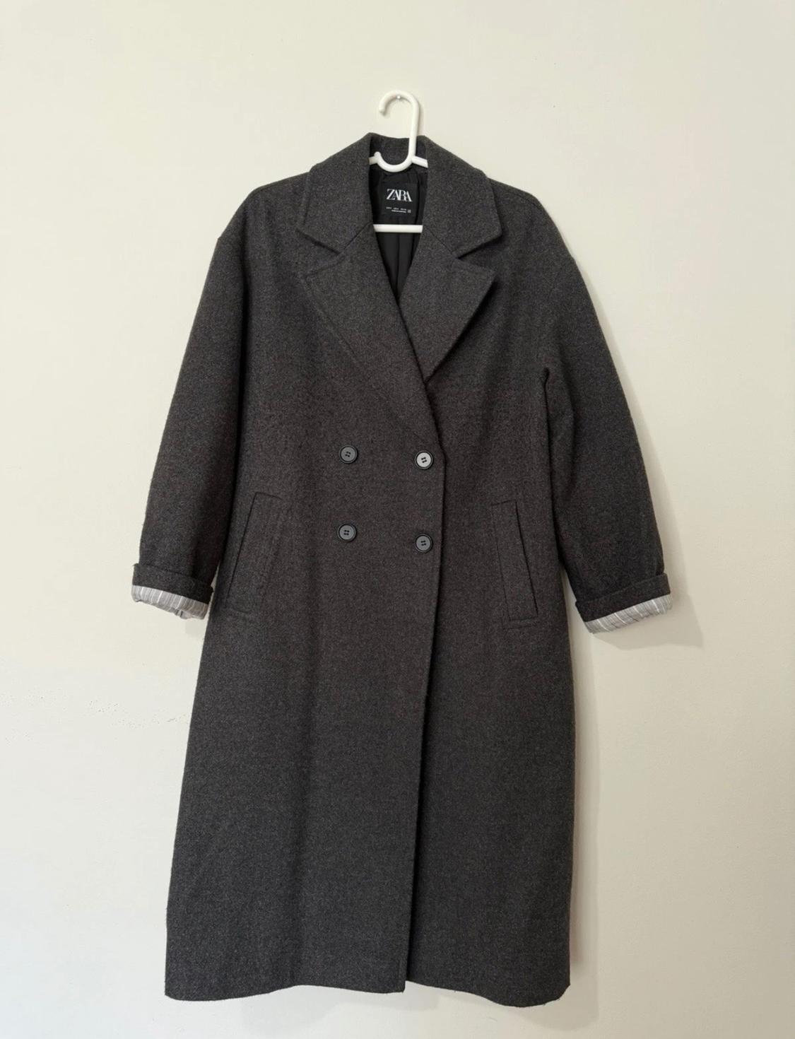 Dark gray wool coat hanging on a white hanger, with a double-breasted design and wide lapels. Visible tag: ZARA.