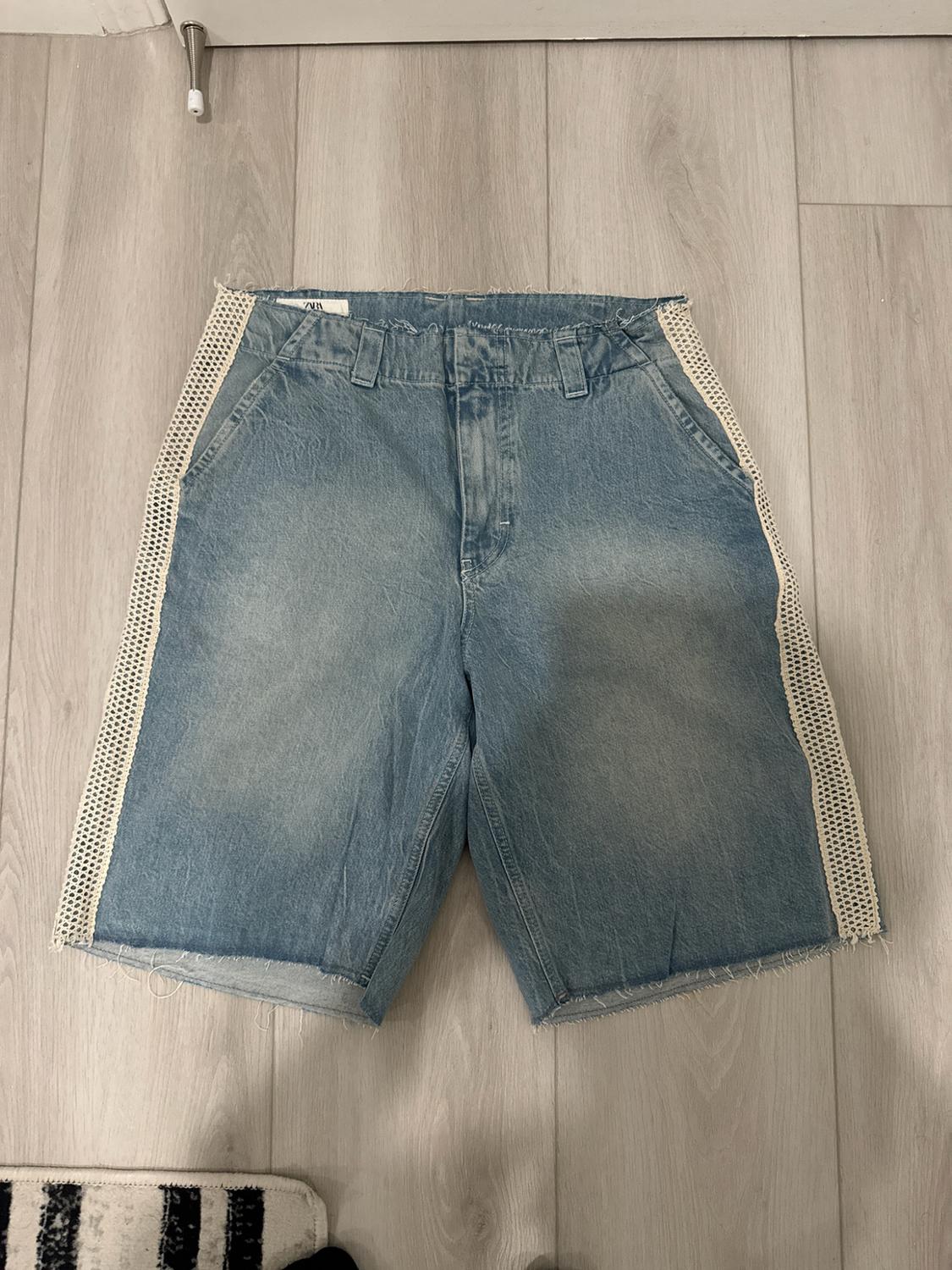 Cowboy Bermuda shorts on a wooden floor. They feature frayed edges and white mesh side panels.