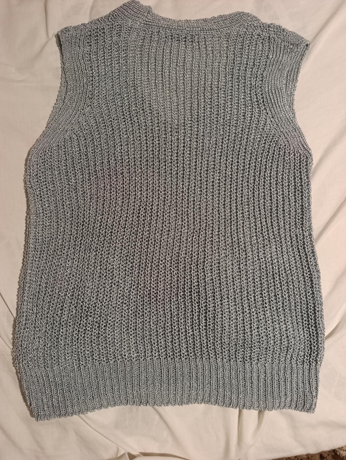 Sleeveless grey knitted vest on a beige surface. Chunky knit design with a round neck and ribbed trim.