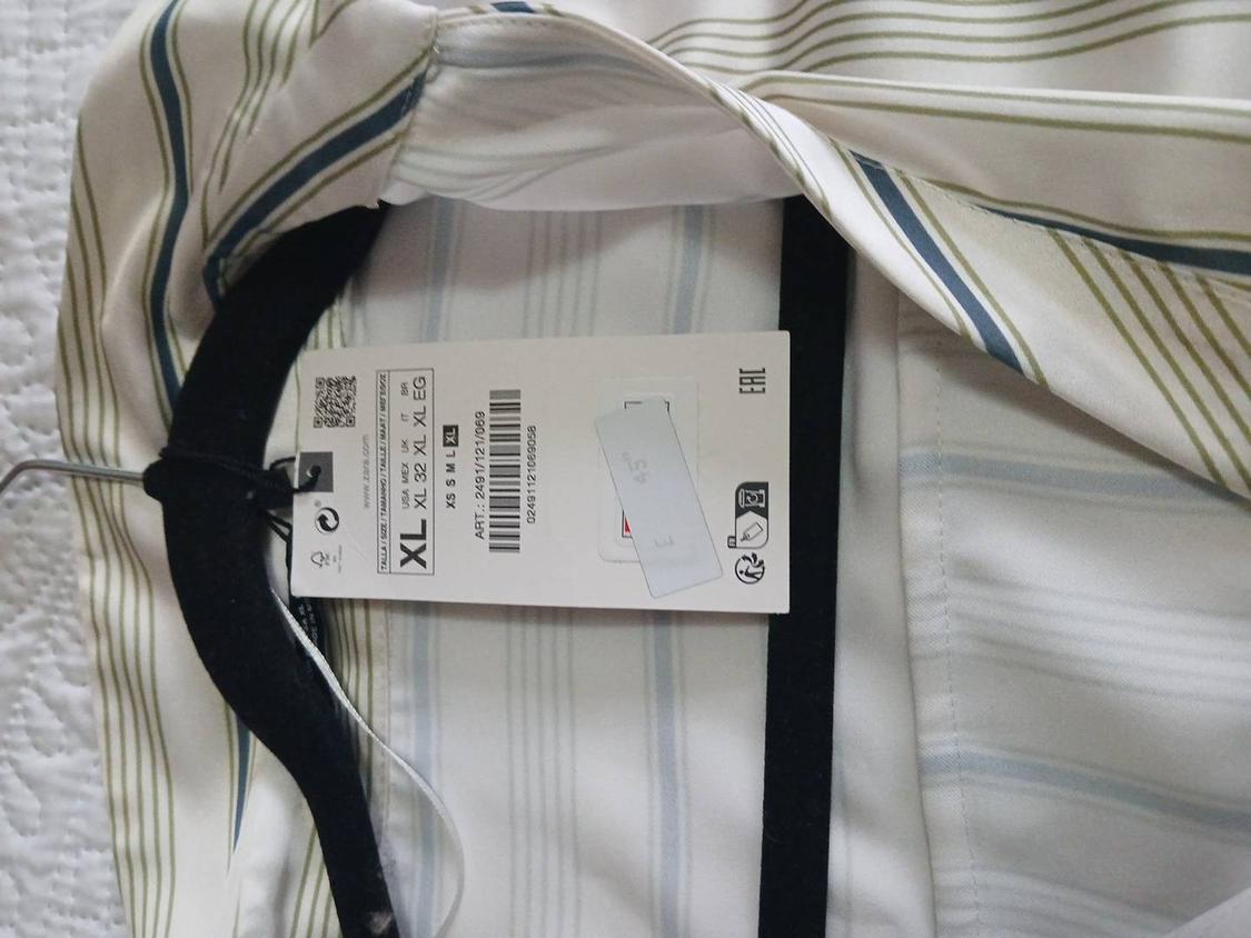 Green and blue striped shirt on a black hanger, with a visible XL size tag. Textured white background.