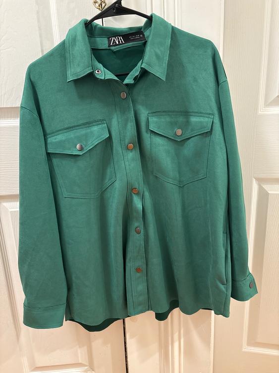 Green long-sleeved shirt with front pockets and metallic buttons, hanging on a hanger. Visible label: ZARA.