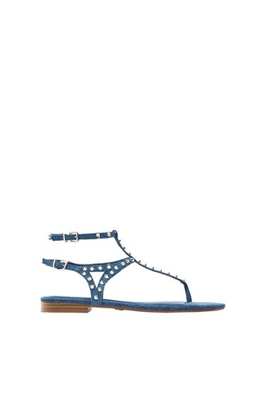 Blue denim flat sandal with straps, silver studs and double buckle fastening on a white background.