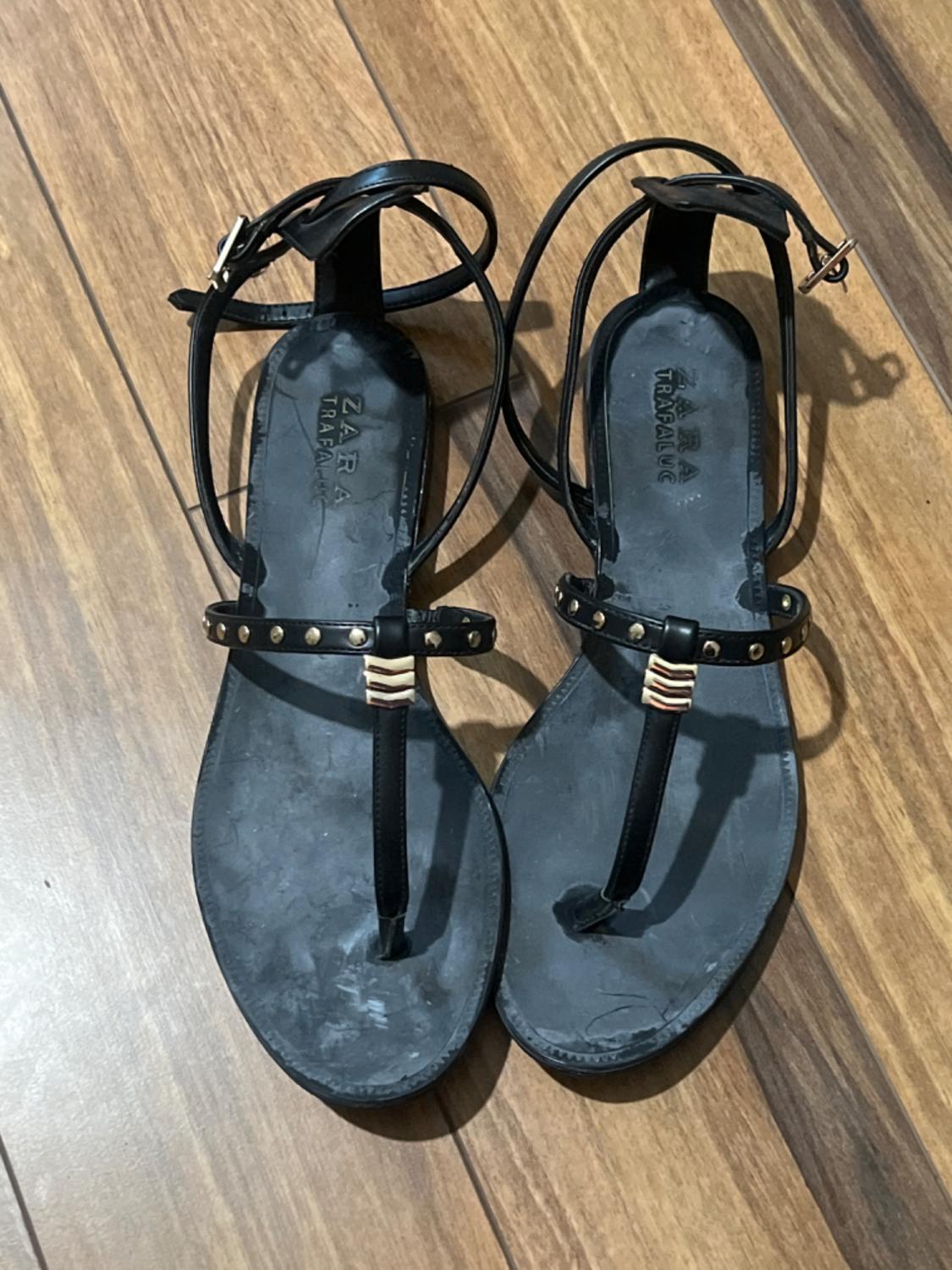 Front view of black sandals with thin straps and gold studs.