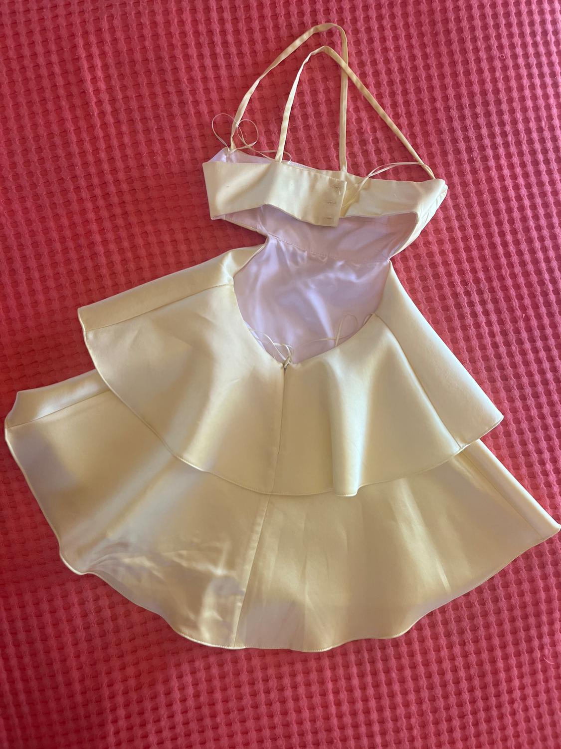 Light yellow mini dress with an open back, spaghetti straps, and a ruffled skirt, against a textured pink fabric background.