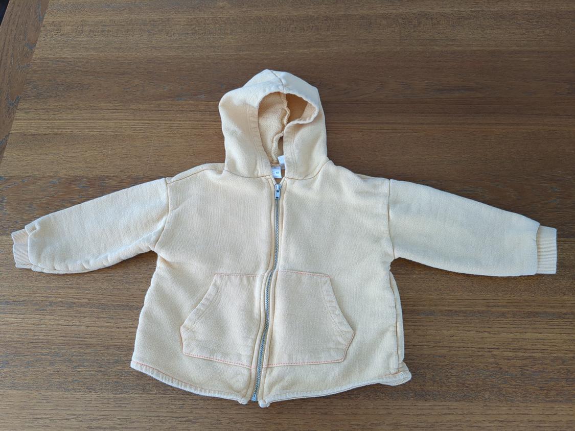 Front view of a beige hooded jacket with front pockets and a zip closure.