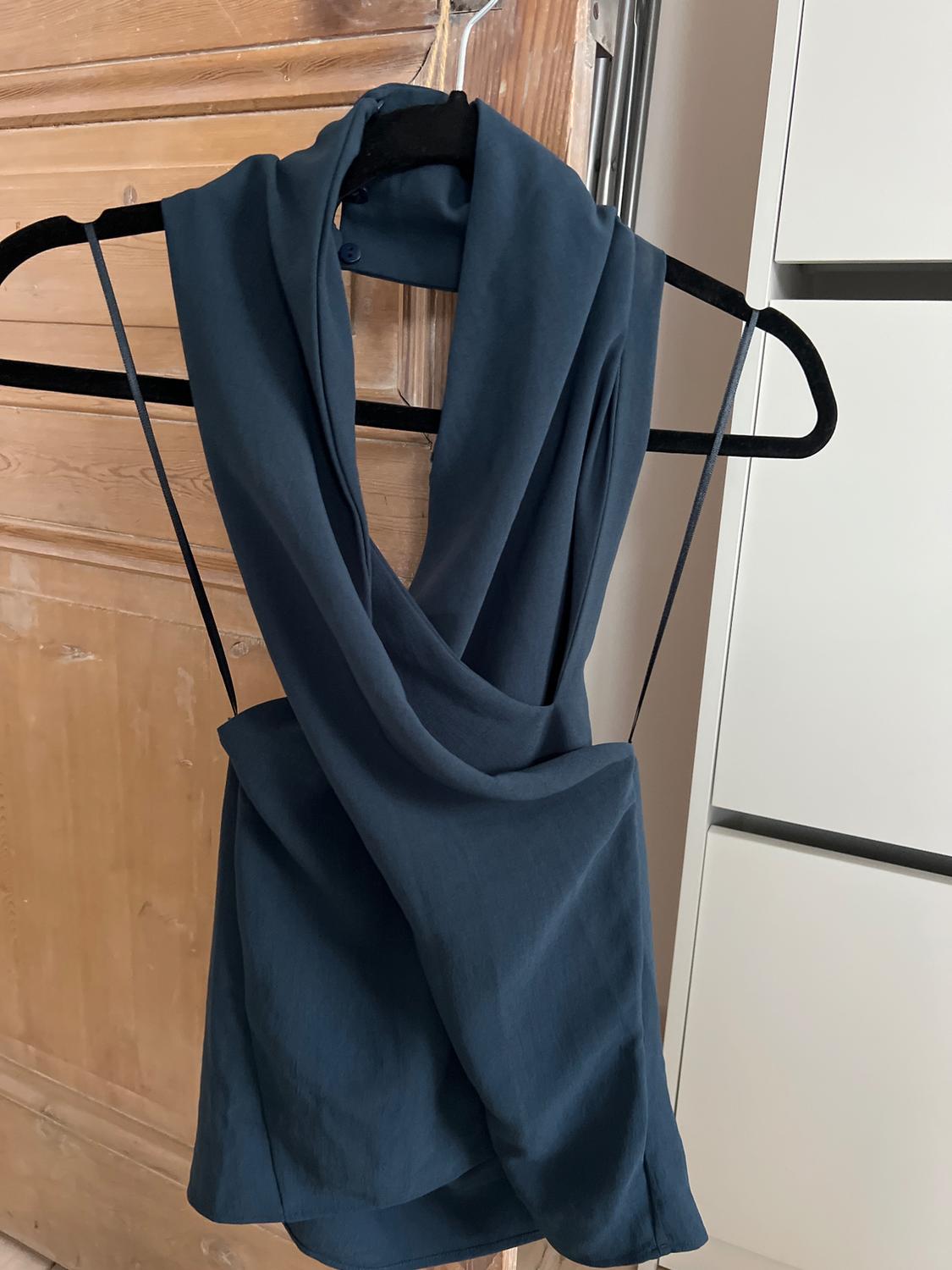 Dark blue top hung on a black hanger, against a light wood background and a white cabinet.
