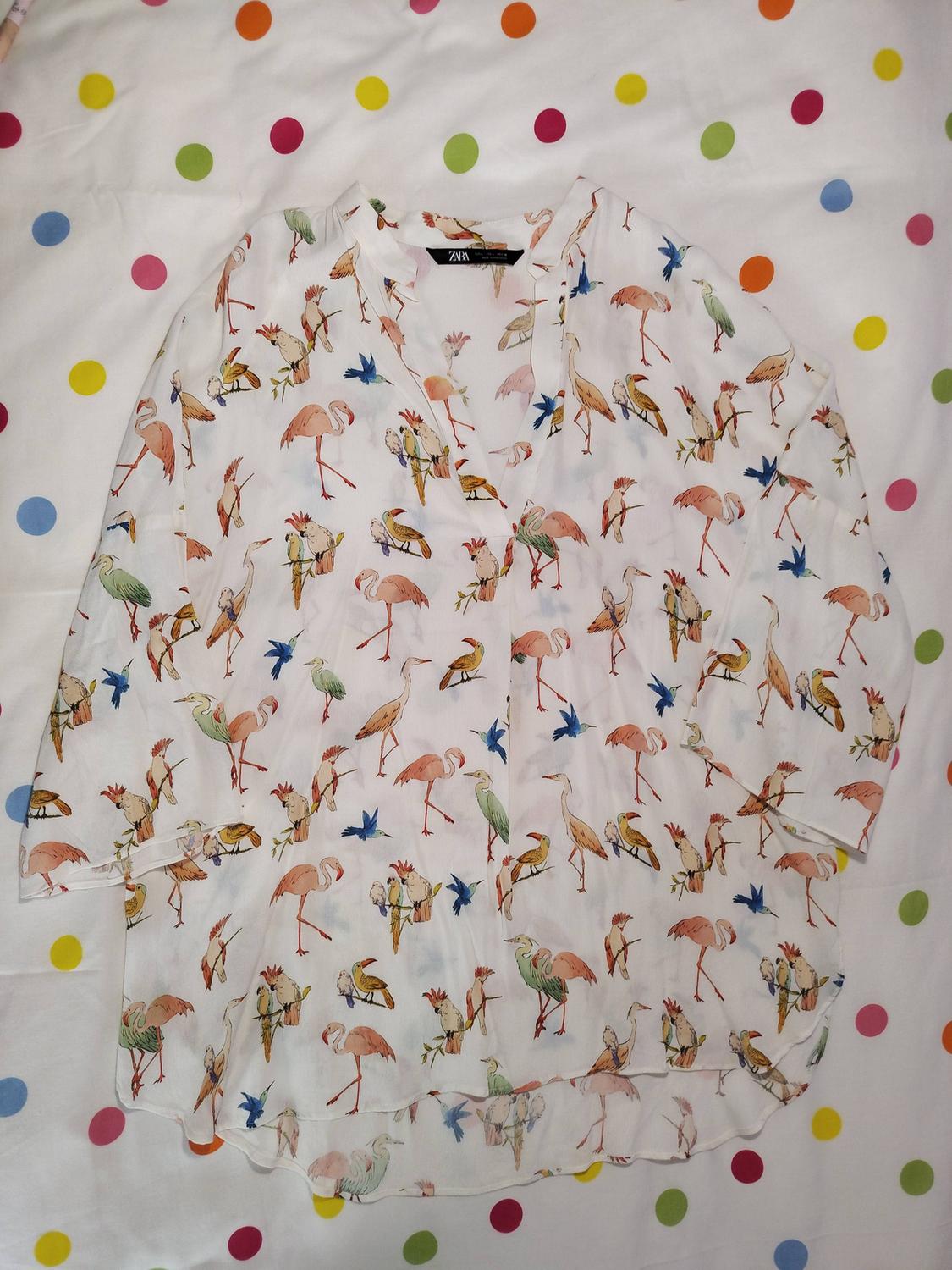 White blouse with a colourful bird print on a multicoloured polka dot background. Visible label with "ZARA" text.