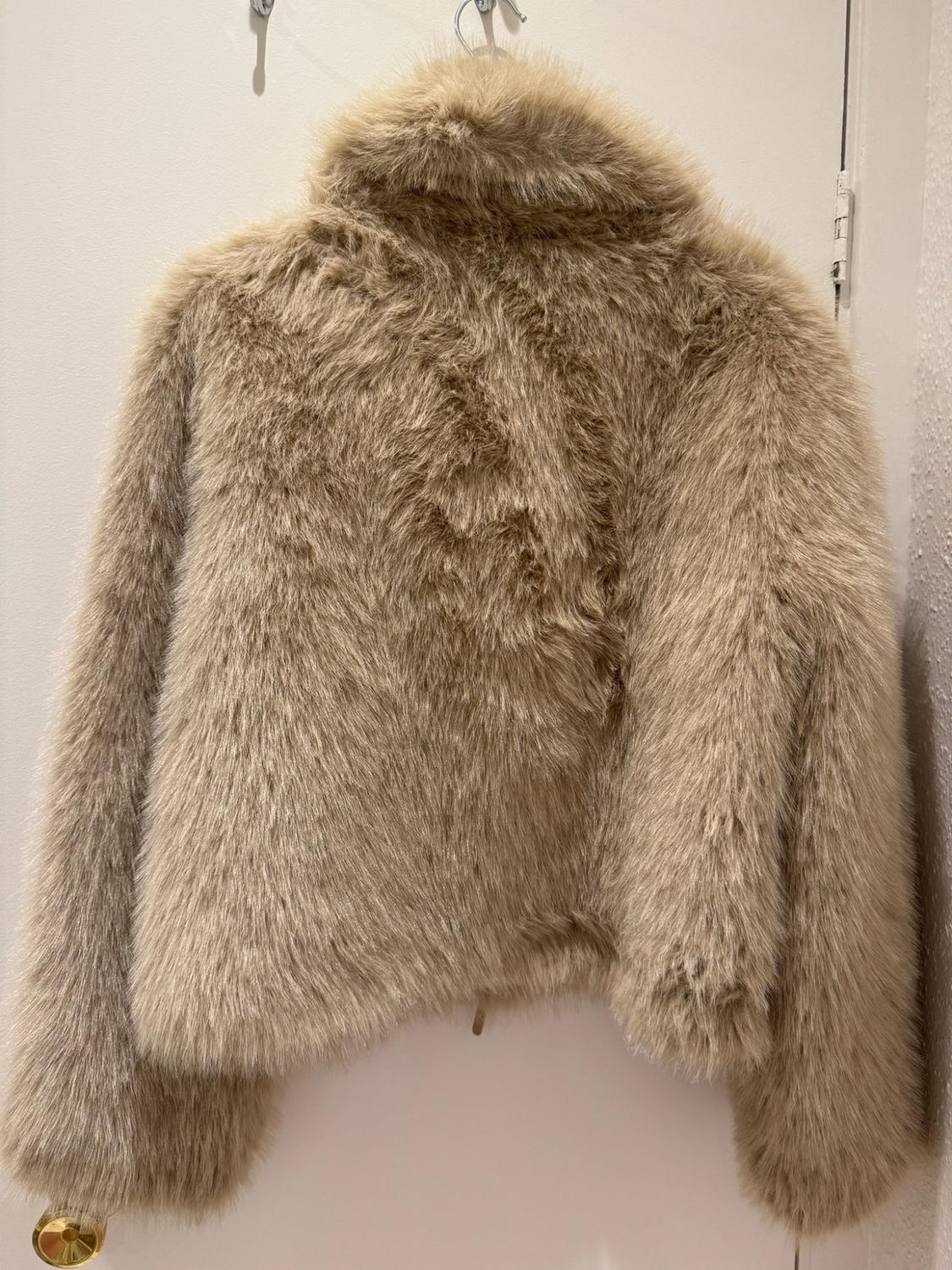 Beige-coloured fur jacket hanging from a coat hook on a white door.