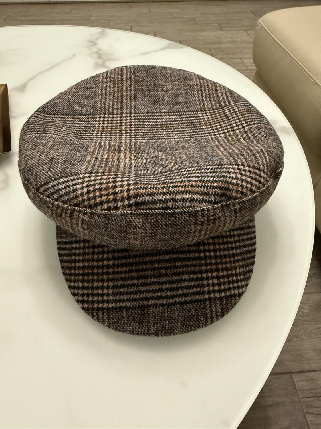 Brown and beige checked fabric cap on a white marble table, with wooden floor and beige sofa in the background.