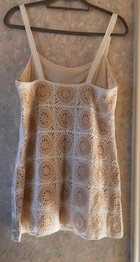Strappy dress on a hanger, with a circular crochet design on a beige background, hanging on a wall with floral wallpaper.