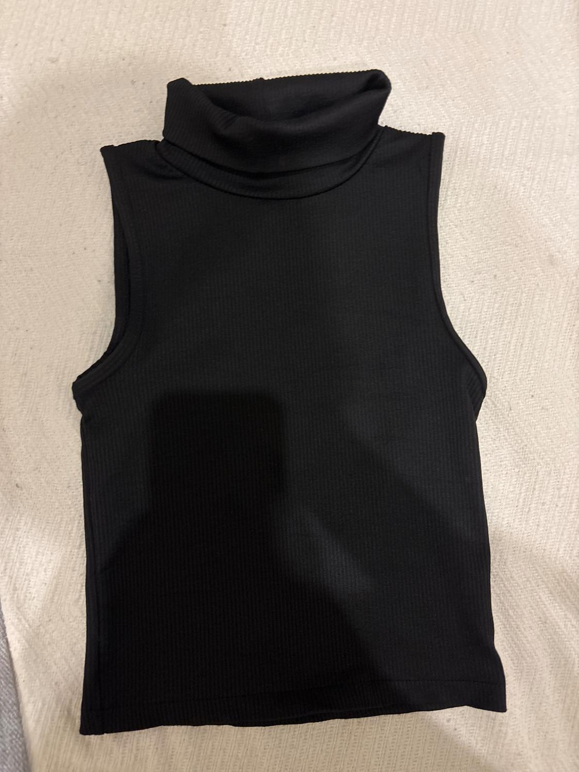 Black sleeveless top with a roll neck on a light textured surface.