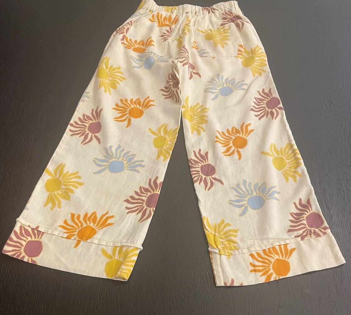 Cream-coloured wide-leg trousers with an elasticated waistband and a print of yellow, orange, blue, and maroon suns on a dark background.