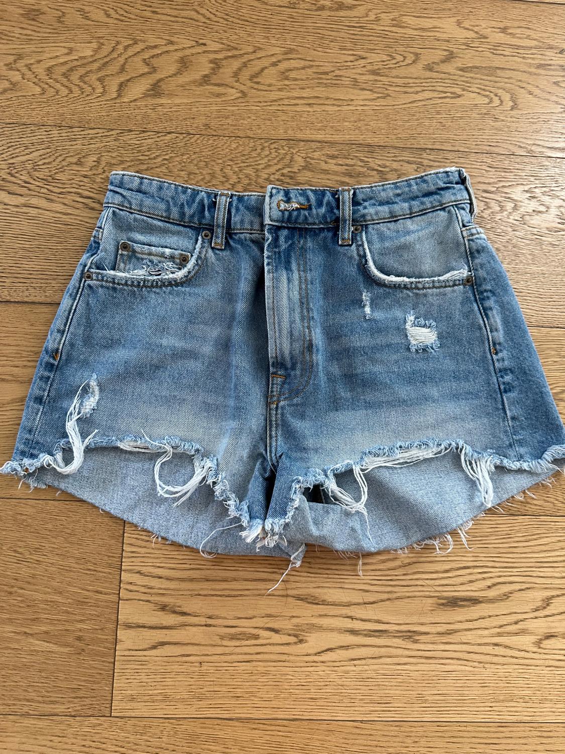Distressed denim shorts with frayed edges on a light wooden floor. Visible front pockets.