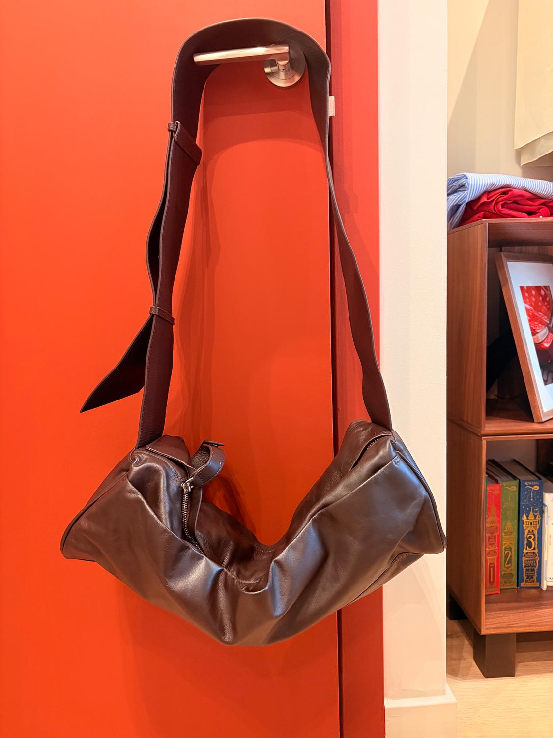Brown handbag hanging from a red door. In the background, a bookshelf with books and a framed photo. Warm and modern atmosphere.